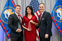 a man and a woman receive an award in front of flags