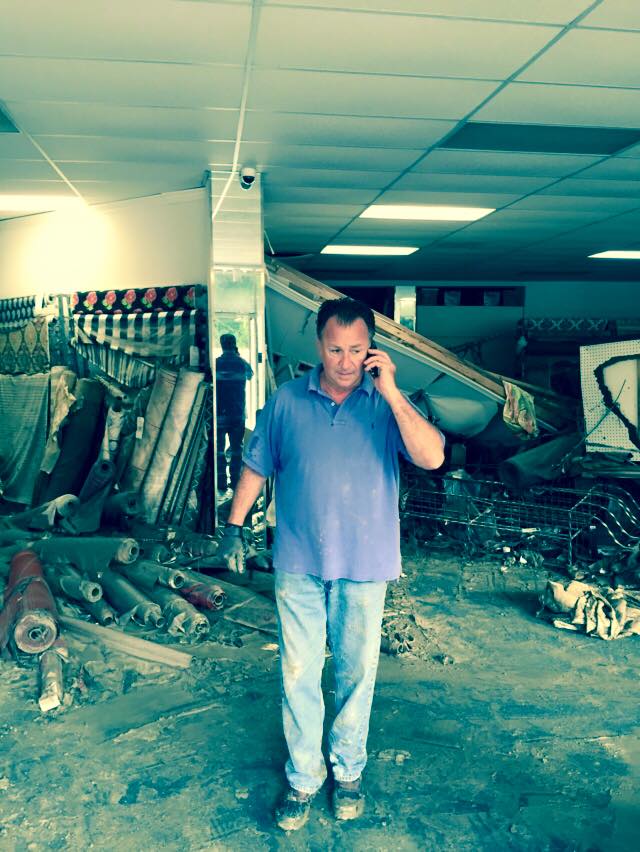 man on the phone in front a store filled with rubble