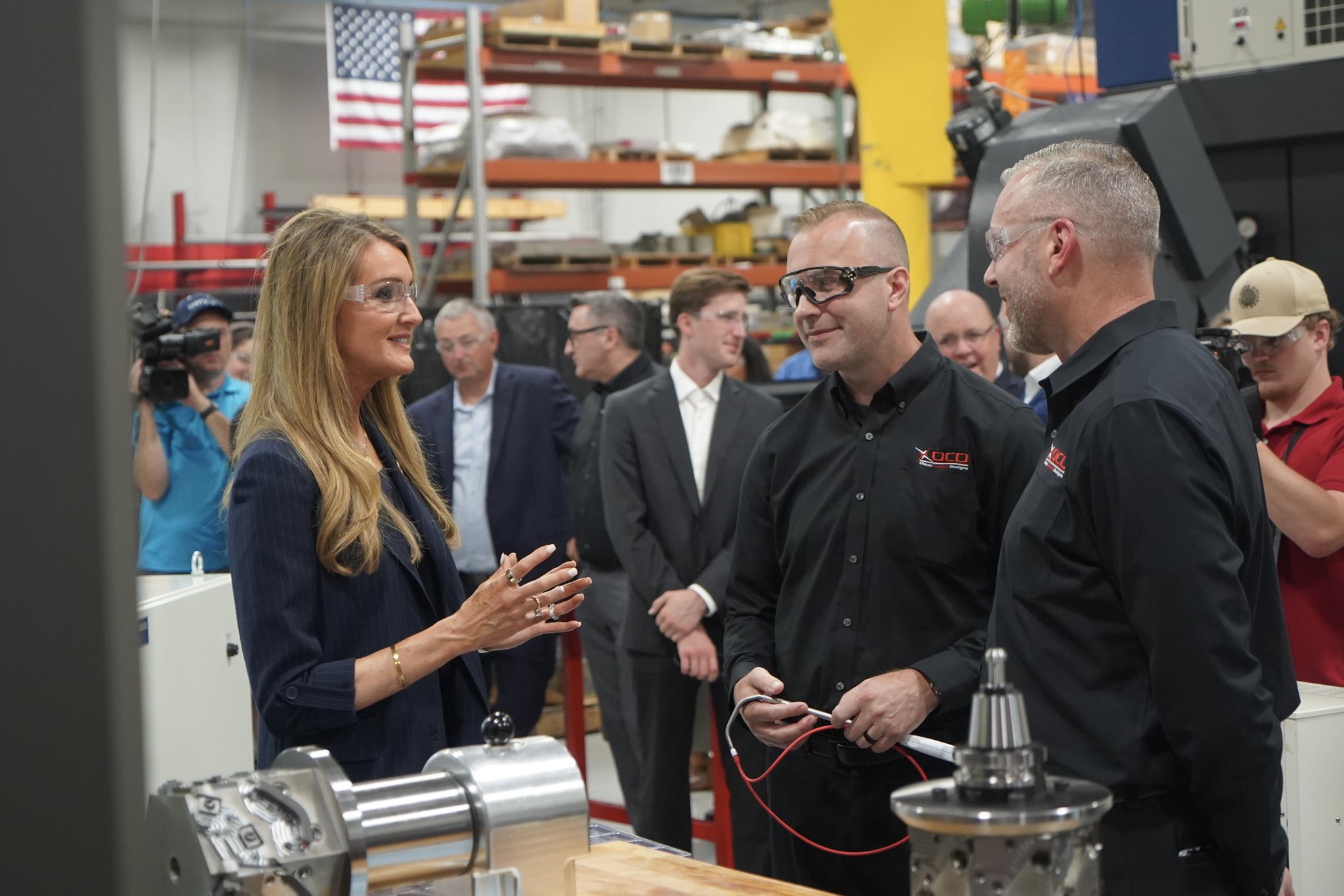 Administrator Loeffler talks with two manufacturing business owners inside of their manufacturing warehouse along with press and SBA staffers