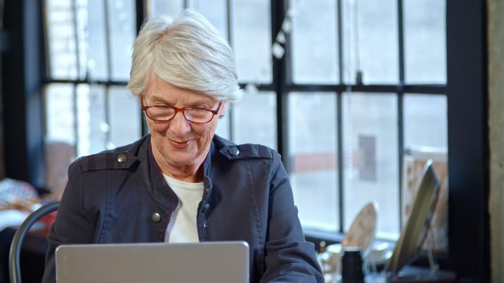 Woman with silver hair and red glasses browsing a laptop