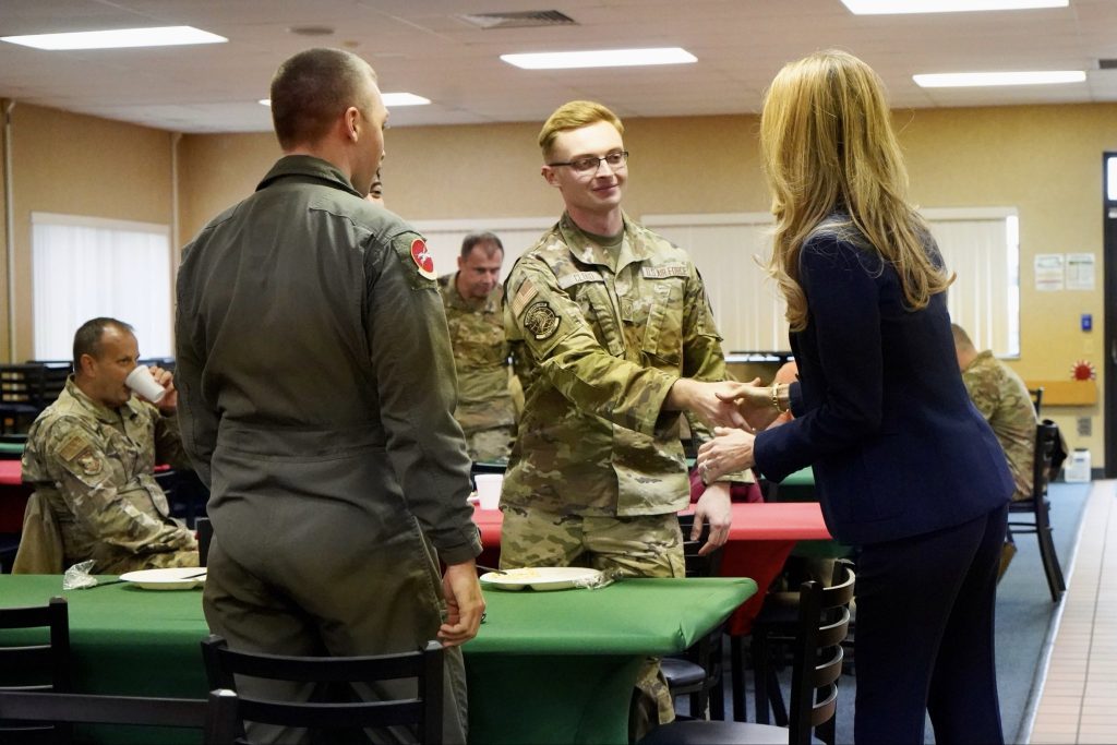 SBA Administrator Loeffler shaking hands with military personnel. Another service member is awaiting a handshake from the Administrator and 3 other servicemen further in the background sitting at tables.
