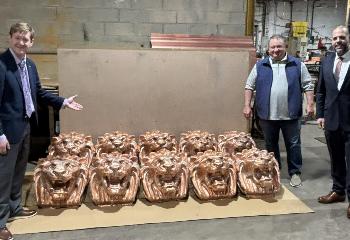 Three people stand in front of metal objects shaped like lions inside a facility.