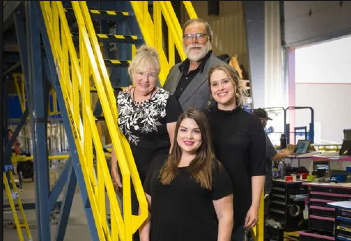 Four people stand in front of a staircase inside a manufacturing facility.