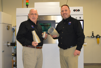 Two people hold products in front of a machine.