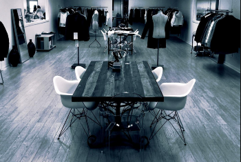 Inside of a display room featuring a table, chairs, and racks of clothes.