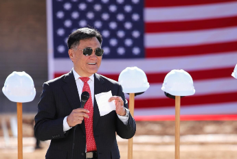 Ki Ho Kang at construction opening ceremony. Shovels with hard hats and an American flag are in the background.