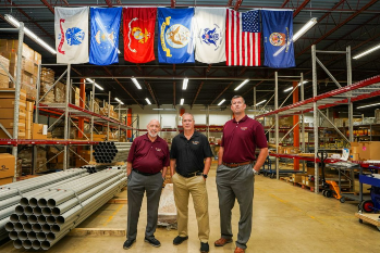 Three men inside warehouse with products and flags hanging from ceiling