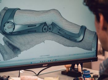 A person using a computer with a large screen displaying a 3D CAD model of a mechanical brace.